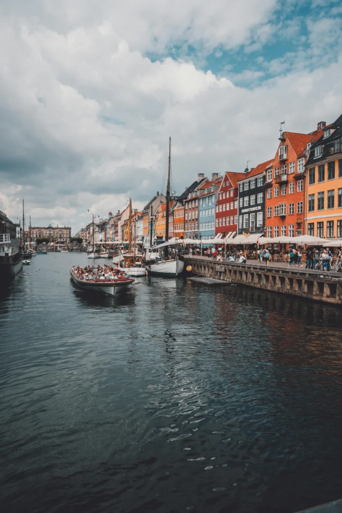 A solo female traveler enjoys the vibrant Nyhavn Canal in Copenhagen, Denmark, with colorful buildings and boats along the waterfront.