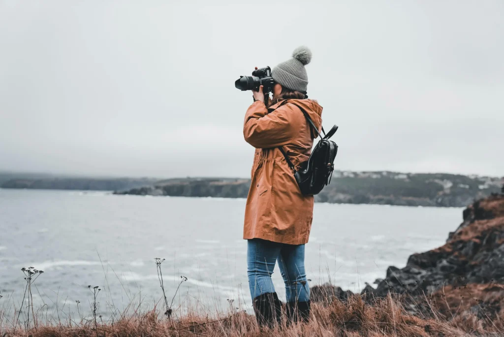 Solo female traveler in winter gear photographing the ocean, embracing adventure and exploration."