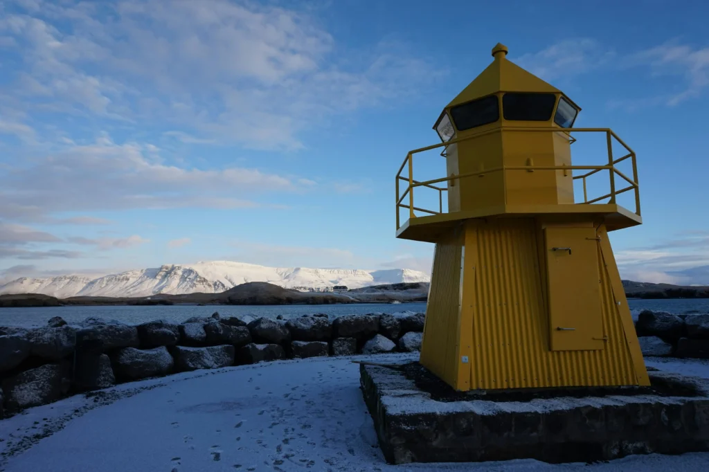 ellow and gray lighthouse in front of mountains, symbolizing an ideal destination for solo female travel.