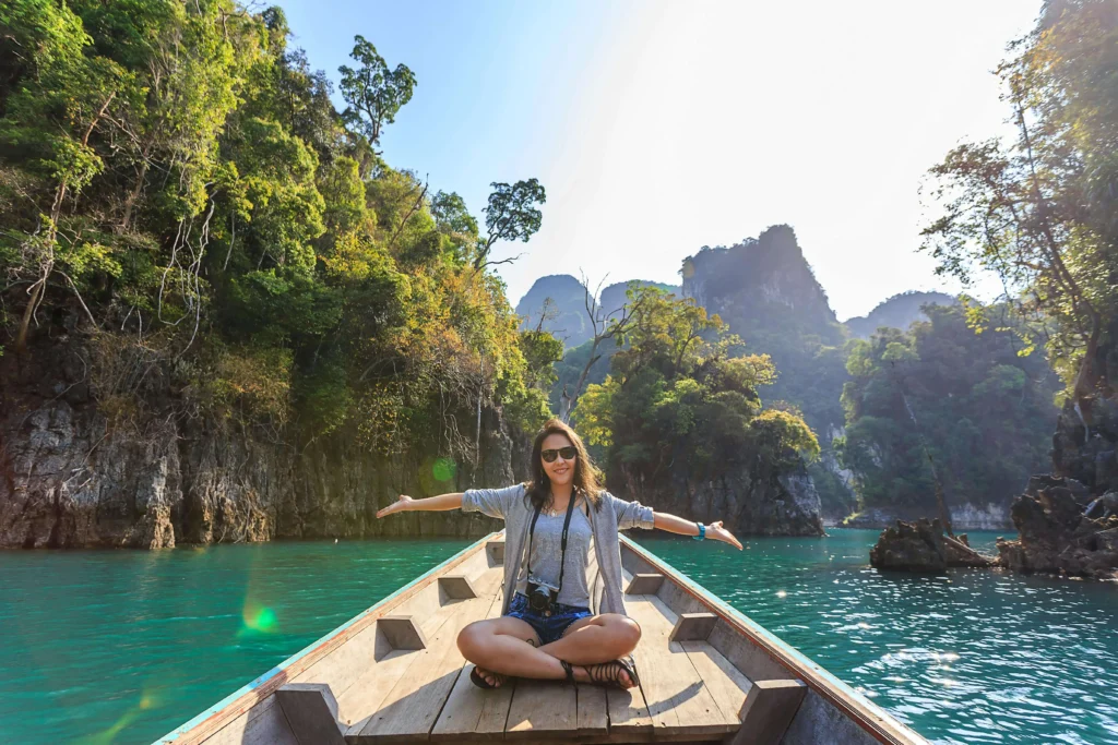 Solo female traveler in a boat, smiling and raising her hands to the sky, enjoying the journey.