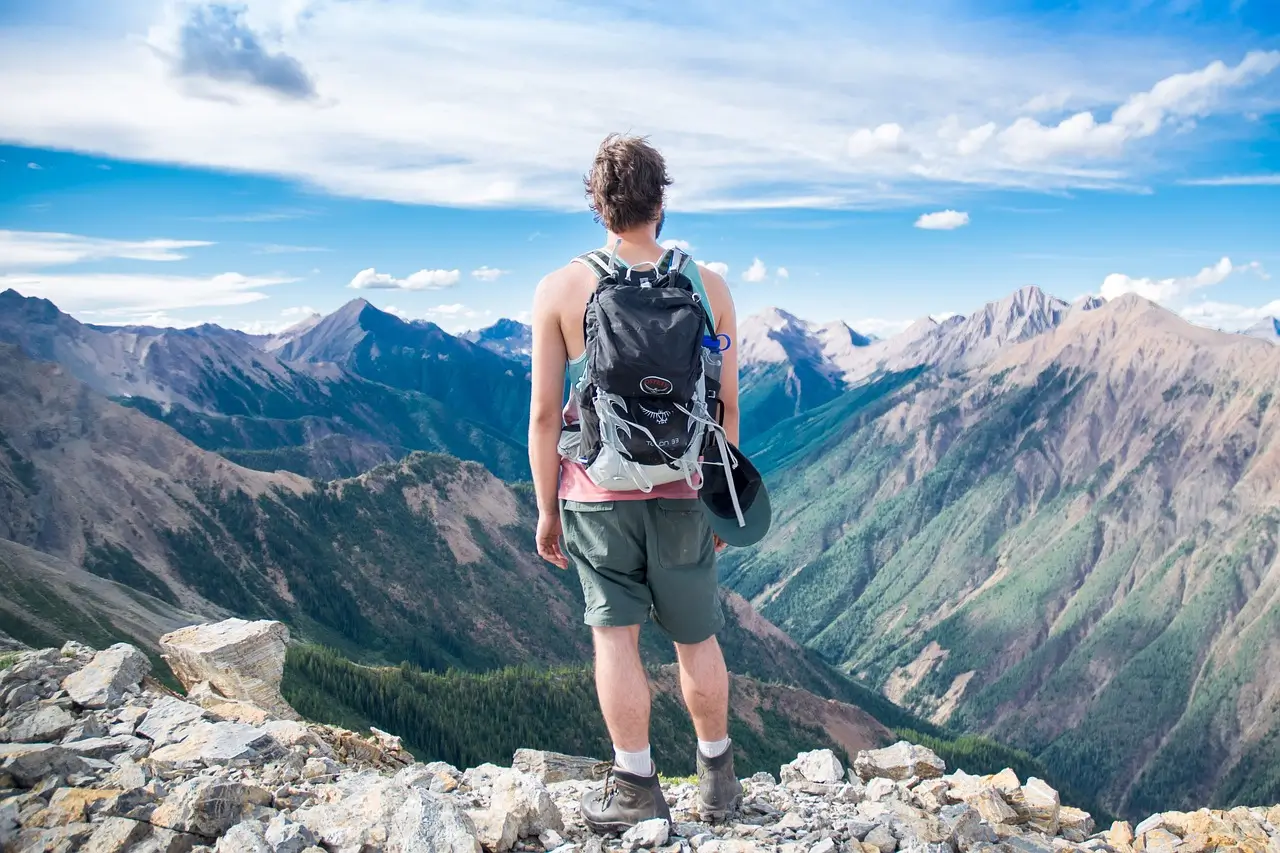 A travel backpack with multiple compartments, sitting on a wooden bench in a scenic outdoor setting, surrounded by green grass and trees in the background.