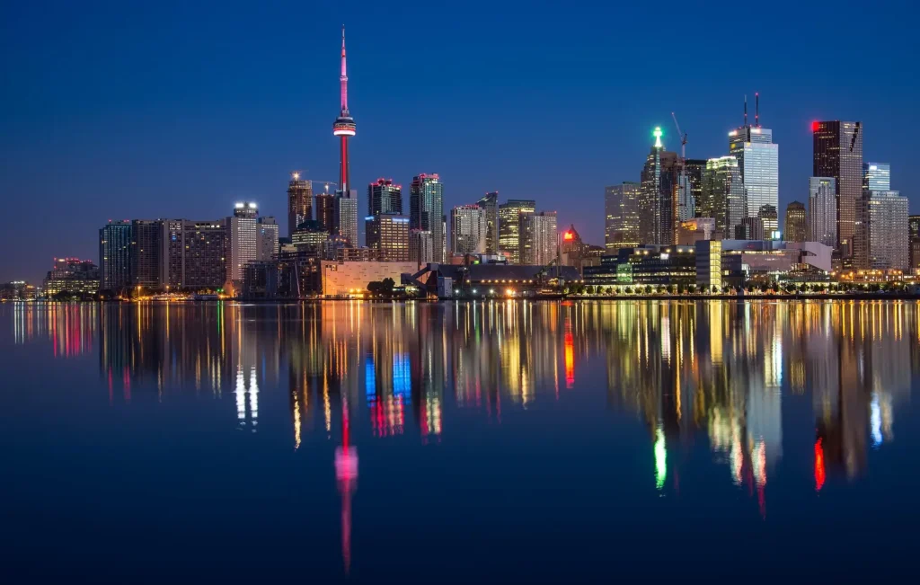 Toronto's CN Tower illuminated at night, reflecting on the waterfront – a highlight of the best city to travel in Canada."