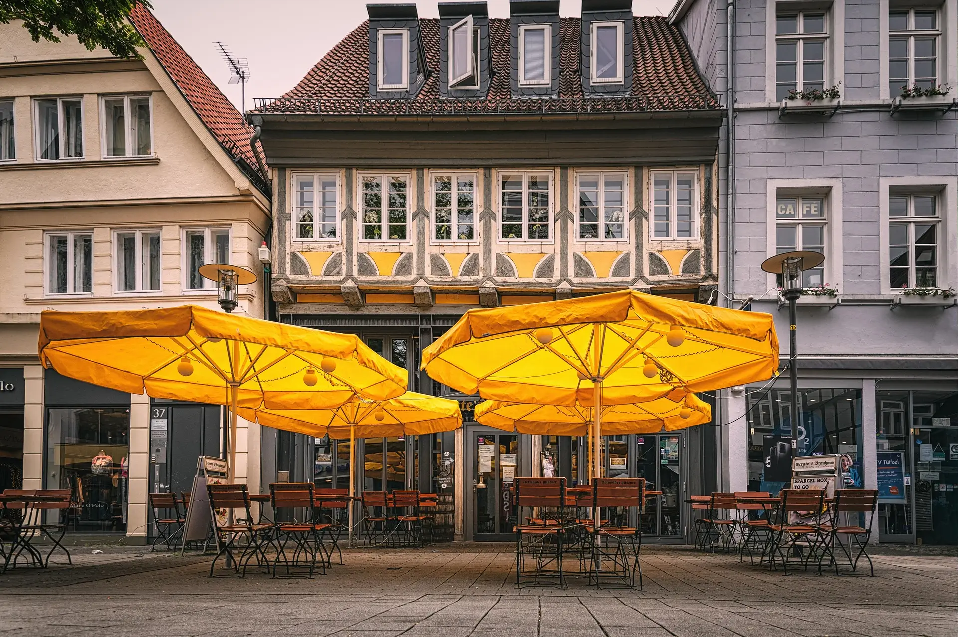 "A bustling city downtown scene featuring a beer garden with parasols, tables, and chairs, set against a vibrant cityscape