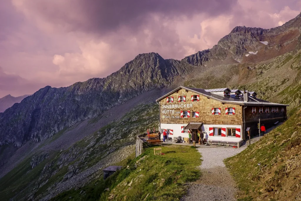 A picturesque travel inn located in the mountains, surrounded by rugged peaks under a dramatic sunset sky