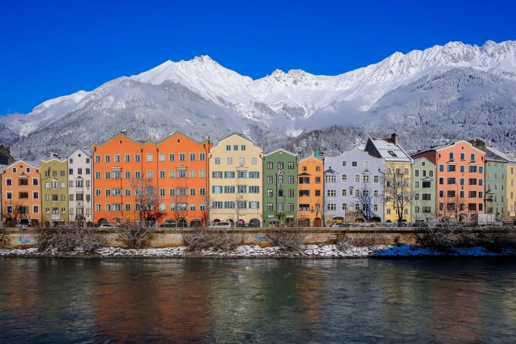 Colorful historic buildings along the Inn River in Innsbruck, Austria, with the Alps in the background