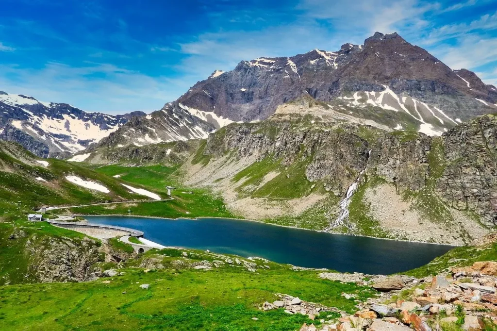  A hiker traversing a rugged alpine trail with towering snow-capped mountains in the background.