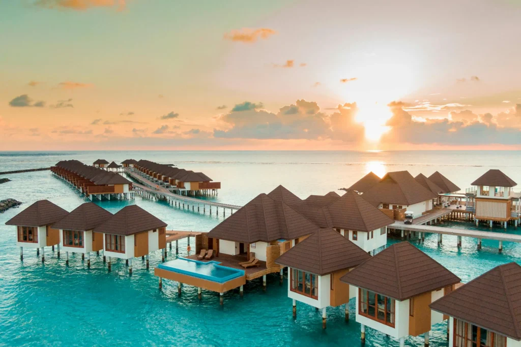 Scenic view of overwater villas on turquoise water with a golden sunset in the background, showcasing one of the best places to travel