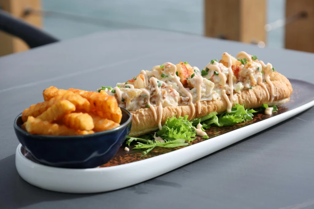 Lobster roll served with crispy fries on a white ceramic plate, showcasing a must-try dish on food tours in America.