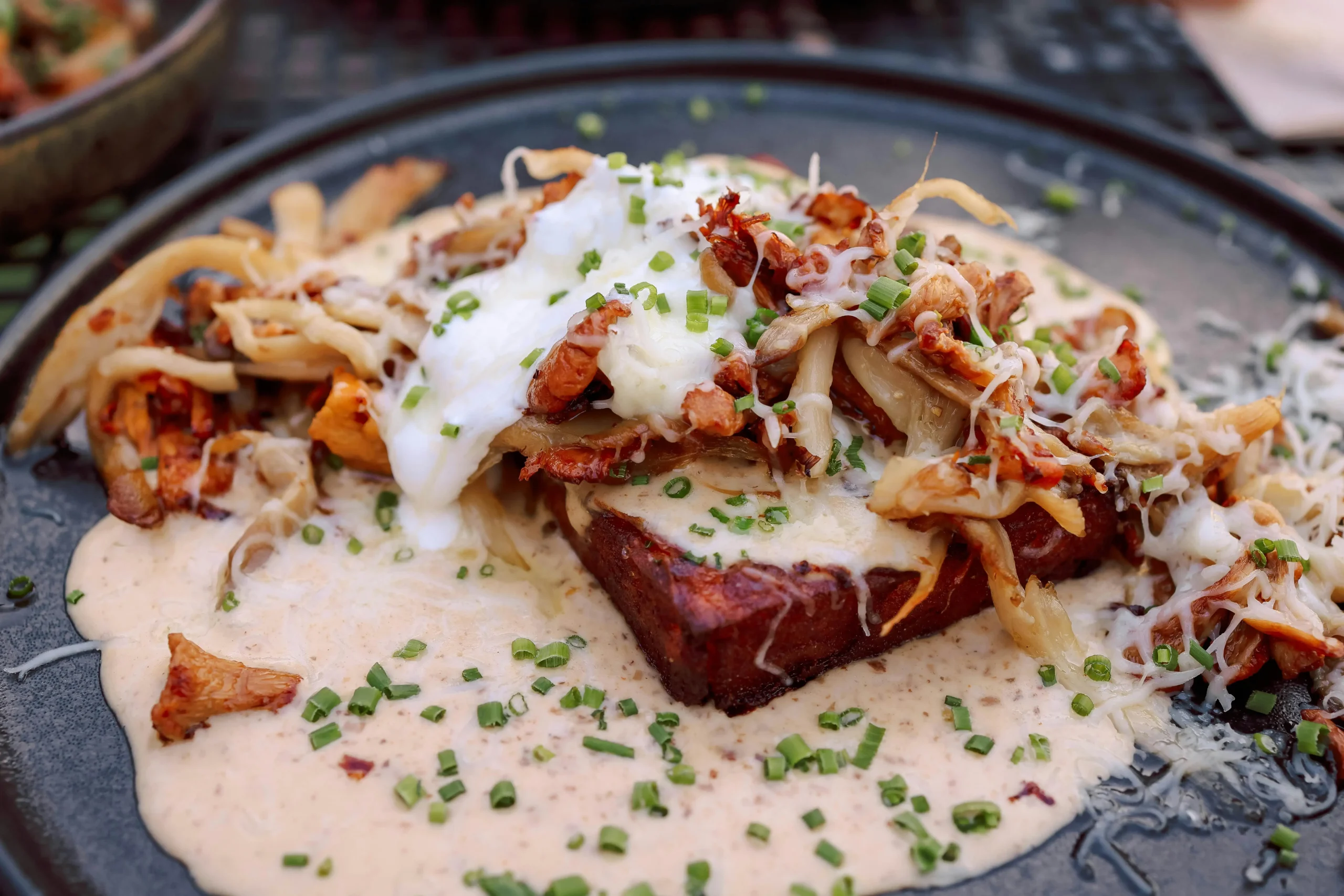 A close-up of a gourmet open-faced sandwich topped with sautéed mushrooms, melted cheese, and fresh herbs, served on a rustic wooden table.