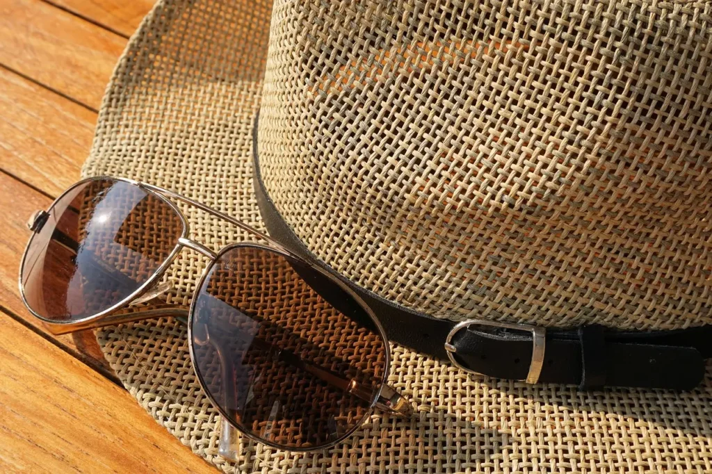 "Sunhat and sunglasses placed on a sandy beach, essential accessories for a family going to the beach."