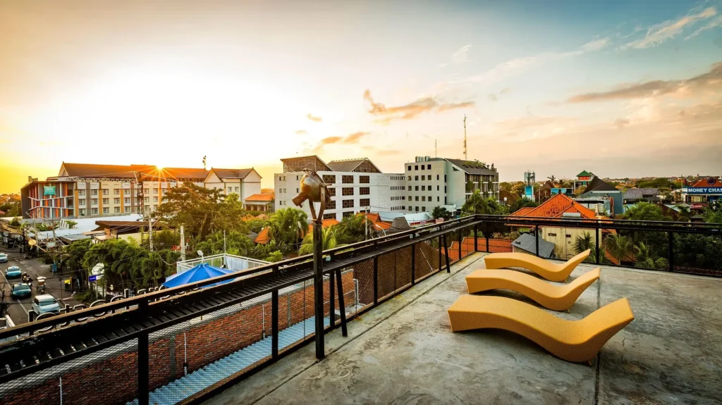 Rooftop view of a travel inn at sunset, overlooking the vibrant cityscape with modern architecture and relaxing lounge chairs.