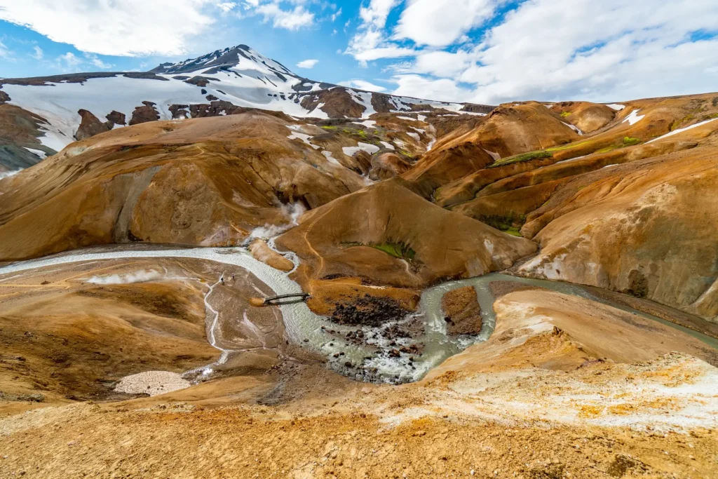 A rugged volcanic landscape featuring sulfur deposits, sandy terrain, and scattered stones under a clear sky.