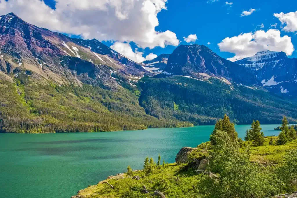 Scenic view of a pristine lake surrounded by towering mountains and lush greenery in Montana, showcasing the natural beauty of one of the best places to stay in Montana.