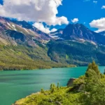 Scenic view of a pristine lake surrounded by towering mountains and lush greenery in Montana, showcasing the natural beauty of one of the best places to stay in Montana.