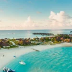 A stunning aerial view of a luxurious island resort in the Maldives, showcasing the ultimate beach aesthetic with crystal-clear waters, white sandy beaches, and tropical overwater bungalows.