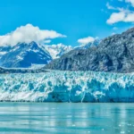 A breathtaking view of a glacier in Alaska, surrounded by towering mountains and clear blue waters, showcasing the natural beauty of one of the best places to live in Alaska.