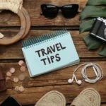 "Travel tips with essential travel items like sunglasses, passport, and camera on the ground."