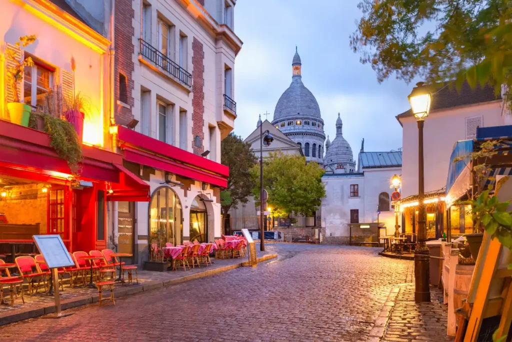 A charming street in Montmartre with a view of the Sacré-Cœur Basilica, glowing with warm lights, capturing the beauty of Paris in December.