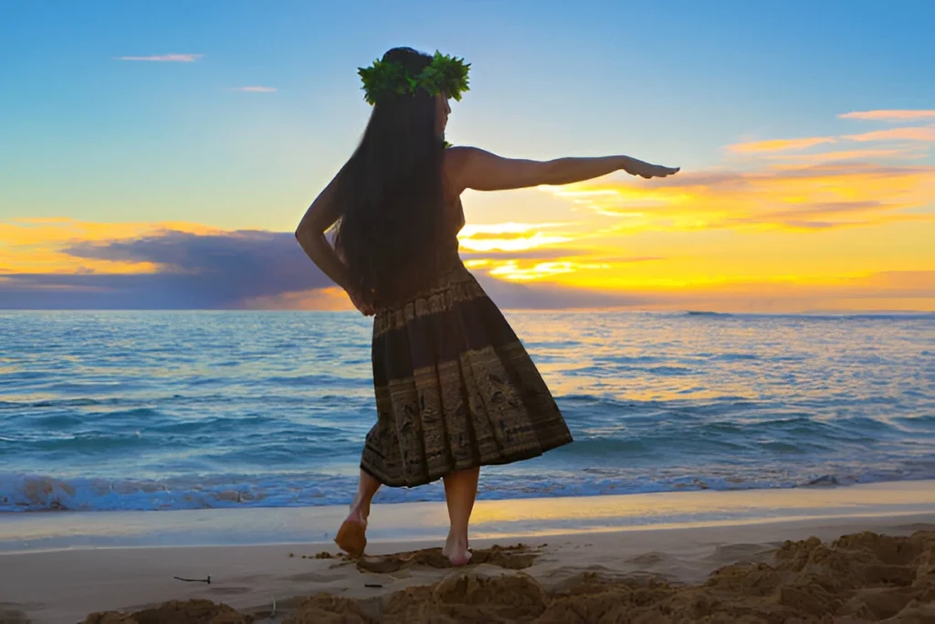 Hawaiian hula dancer in traditional luau attire dancing on a tropical beach at sunset in Kauai, Hawaii.