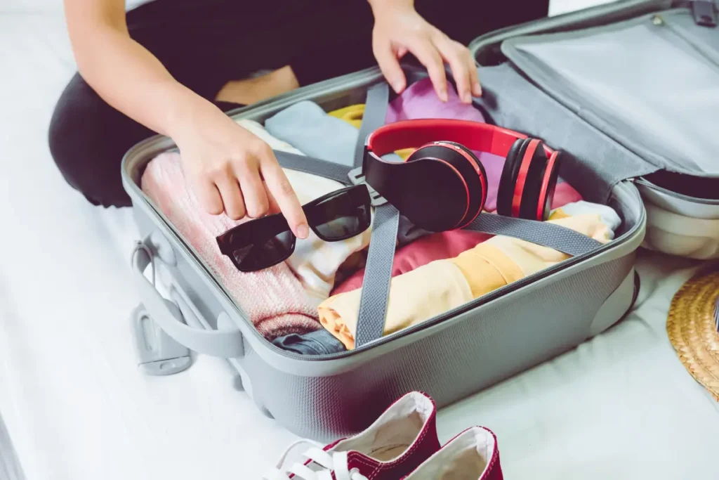 Traveler packing essential accessories for a trip, including a passport, sunglasses, and a travel wallet.