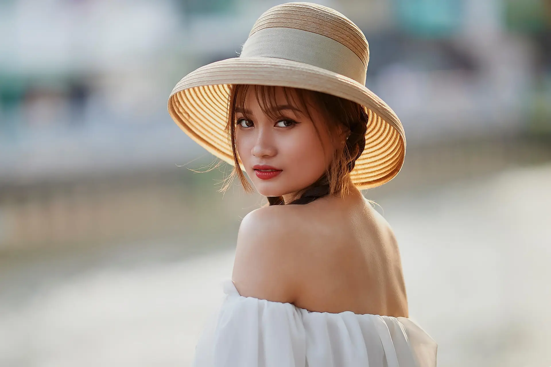 A stylish woman wearing a lightweight off-shoulder dress and a wide-brimmed hat, perfect for tropical climates, illustrating the best travel fast drying clothes for Asia.