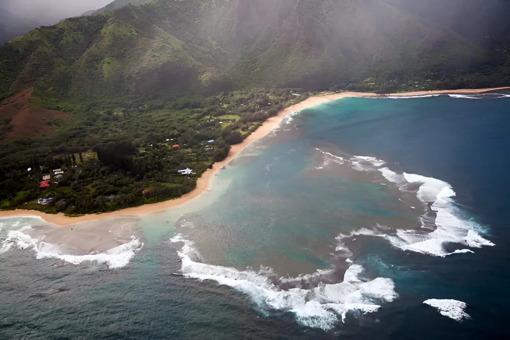 "Aerial view of surf breaking over a reef near Hanalei Bay, showcasing one of the best places to stay in Kauai with breathtaking coastal views."

