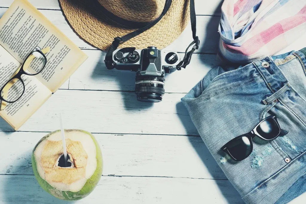 Travel aesthetic: summer essentials including a book, glasses, hat, and camera."