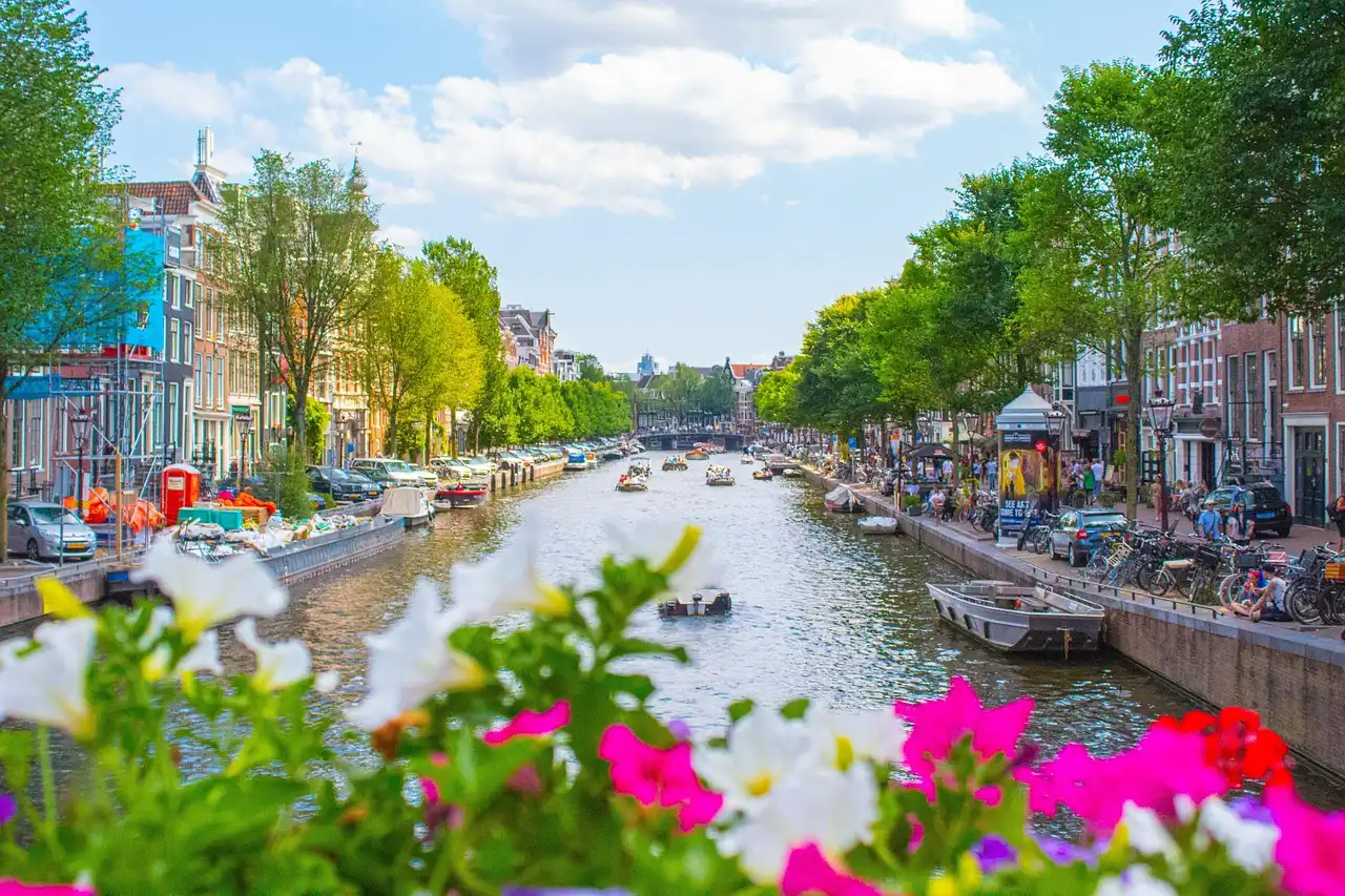 "Sunny day in Amsterdam with clear blue skies, blooming flowers, and boats on the canal, illustrating the pleasant Amsterdam weather for May."