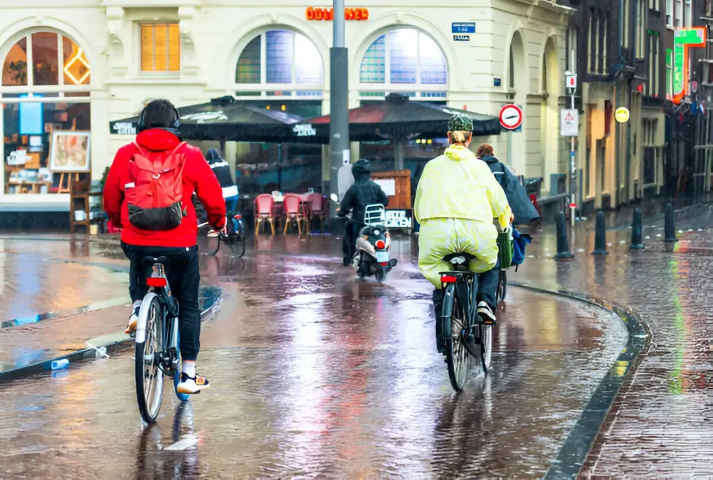 "Cyclists in Amsterdam riding through the city center during a heavy downpour, showcasing the unpredictable Amsterdam weather for May."