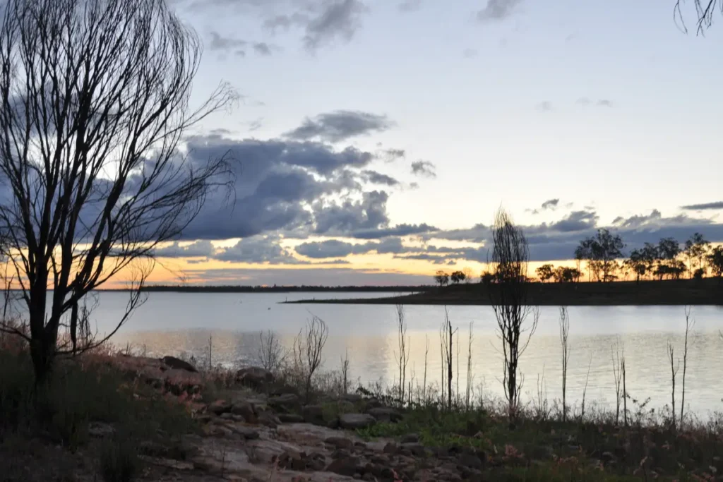 A tranquil lakeside sunset near Fairburn Family Travel Center with silhouetted trees and calm water.