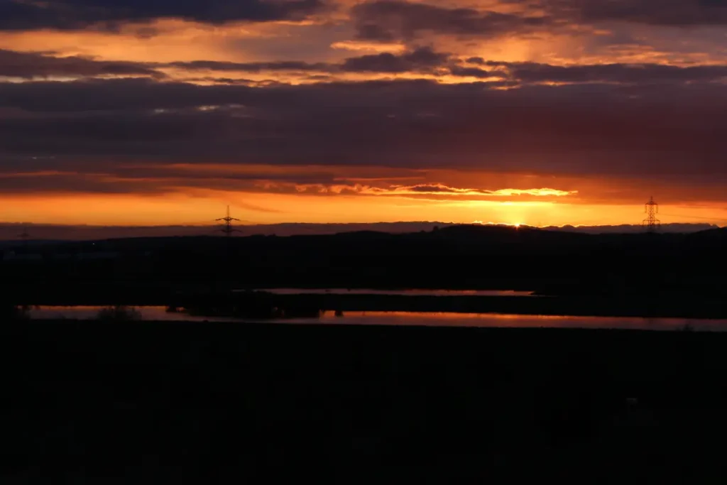 A dramatic orange sky near Fairburn Family Travel Center at sunset, with silhouettes of distant trees and power lines.