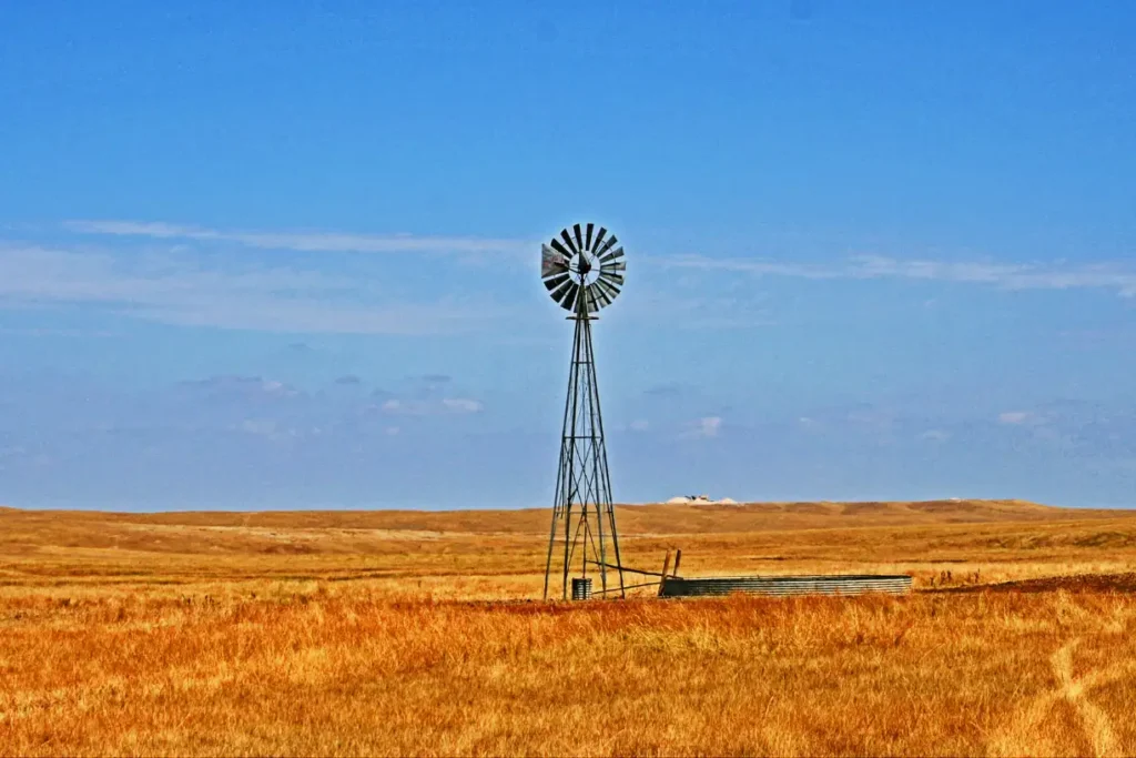 A scenic rural landscape near Fairburn Family Travel Center, featuring a classic windmill standing tall against a vast golden prairie under a bright blue sky.